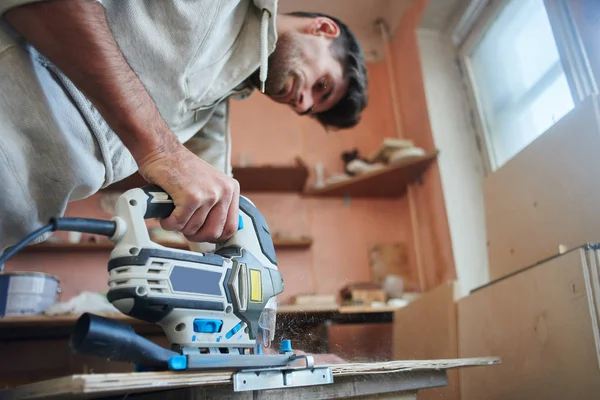 Young man working with electric fretsaw while sawing plywood, concept of make repairs in apartment — Stock Image Young Man Working Electric Fretsaw While Sawing Plywood Concept Make Stock Photo