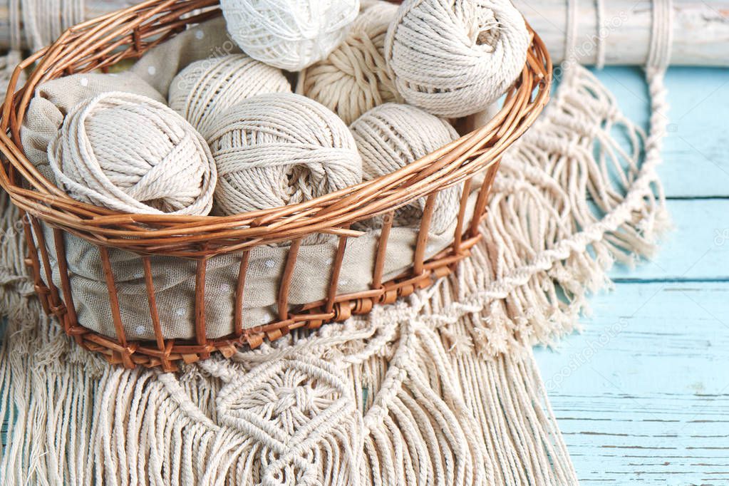 Handmade macrame braiding with threads in basket on wooden background, close-up