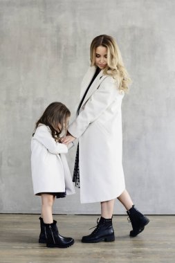 Anne ve kızı sıcak aynı beyaz kat elele duran beton duvar arka planda, lookbook kavram olarak