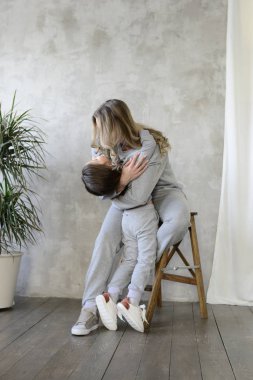 şirin kız gri yumuşak eşofman ve spor ayakkabı Studio, lookbook kavramı ahşap sandalye üzerinde anne sarılma 