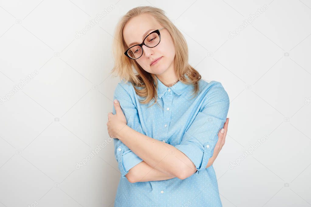 unhappy woman in blue shirt embracing herself isolated on white background