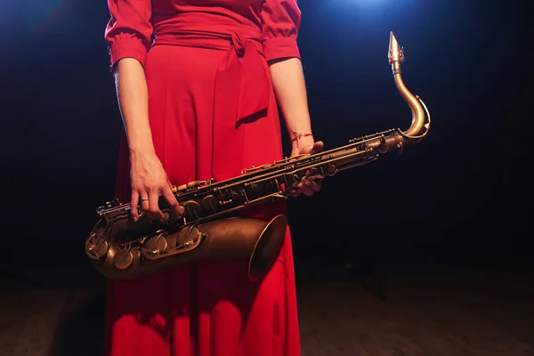 Musician woman in bright red dress holding saxophone in hands, close-up