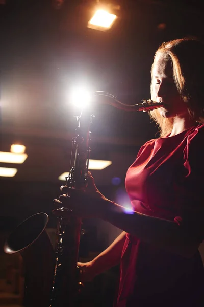 音乐家妇女在红色礼服演奏萨克斯在黑暗的阶段 — 图库照片