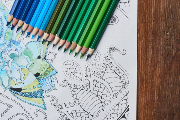 coloring page with pencils in blue and green colors on wooden table , close-up
