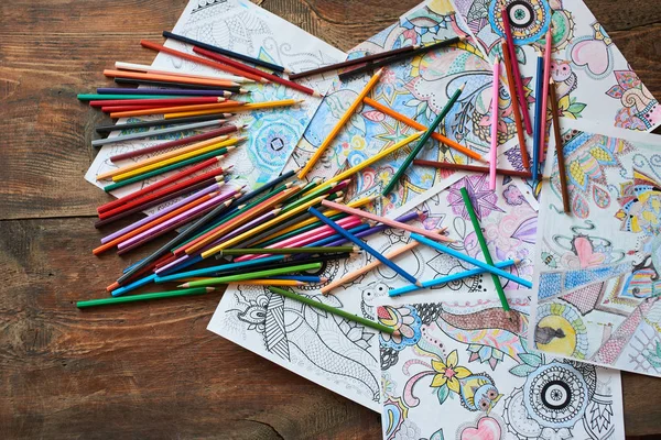 coloring pages with bright pencils on wooden table, top view