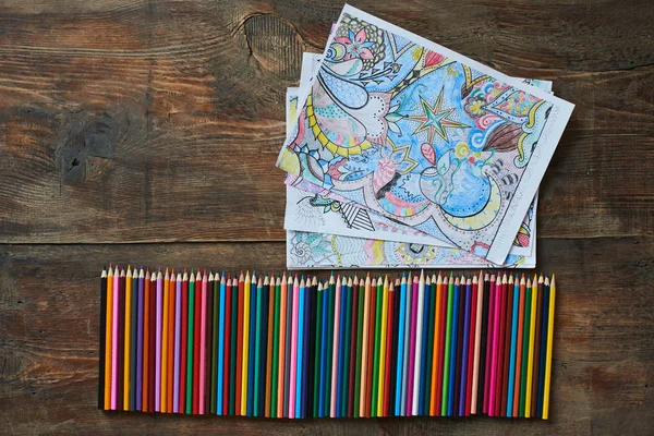 row of pencils with collection of coloring pages on table, close-up
