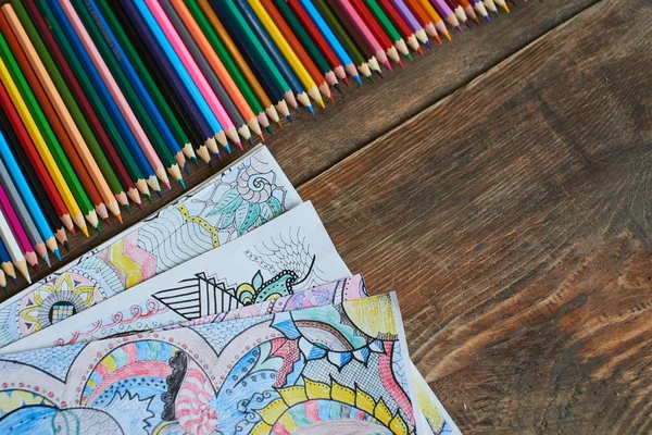 row of pencils with collection of coloring pages on table, close-up