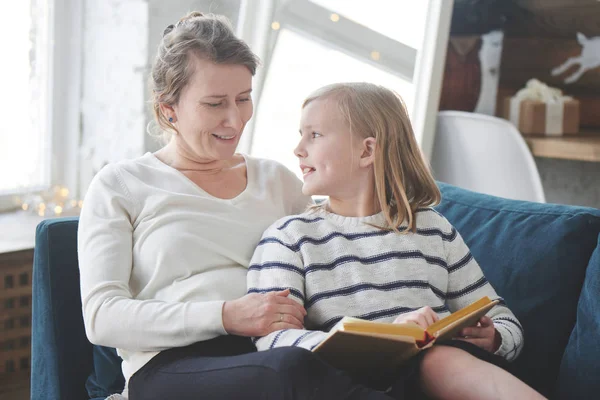 Figlia Lettura Libro Mentre Seduto Con Mamma Sul Divano Appartamento — Foto Stock