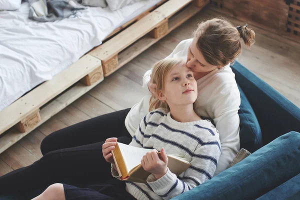 Filha Leitura Livro Enquanto Sentado Com Mãe Sofá Apartamento — Fotografia de Stock