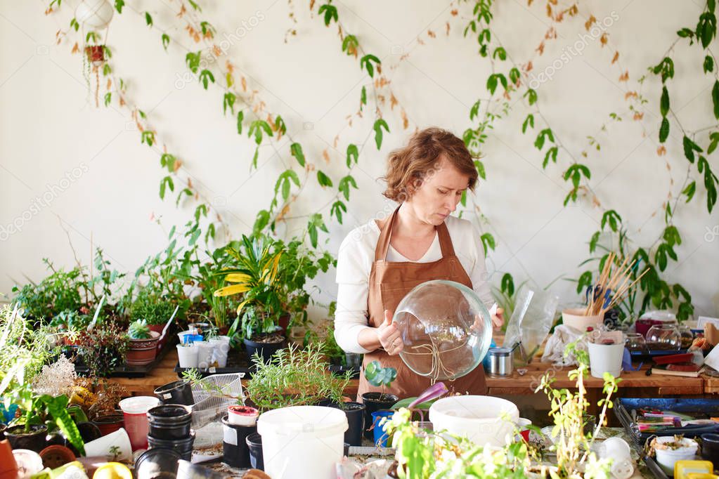 female florist holding round shaped glass mini terrarium and choosing plants 
