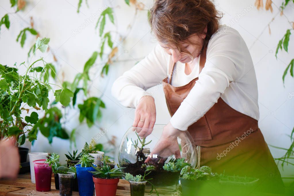 Woman florist growing house plants and flowers in mini terrarium, female hobby concept 
