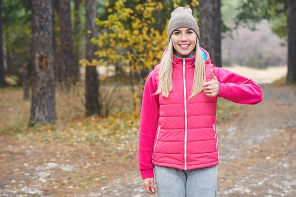 Blonde Woman Warm Sportswear Showing Thumb While Standing Autumn Forest — Stock Photo, Image