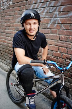 yakışıklı bisikletçi döngüsü üzerinde oturan ve kırmızı tuğla zemin üzerine bina ile kamera yan sokakta bakarak Güvenlik kask 