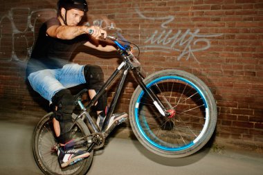 kırmızı tuğla binanın duvarının yakınında çabayla döngüsünün arka tekerlek üzerinde sürme güçlü yakışıklı bisikletçi 