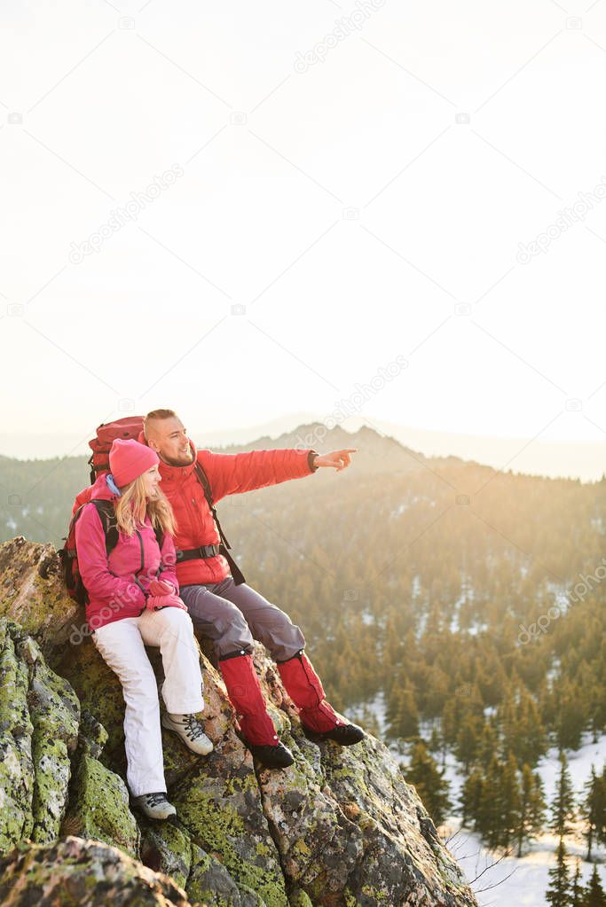  man pointing forward awhile sitting with woman on top of mountain