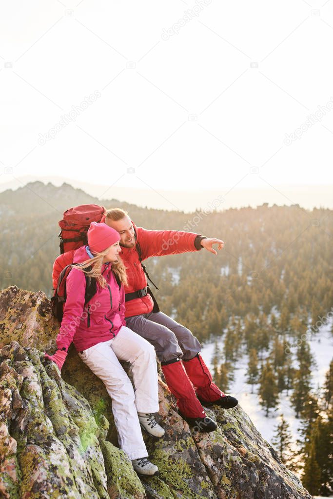  man pointing forward while sitting with woman on top of mountain