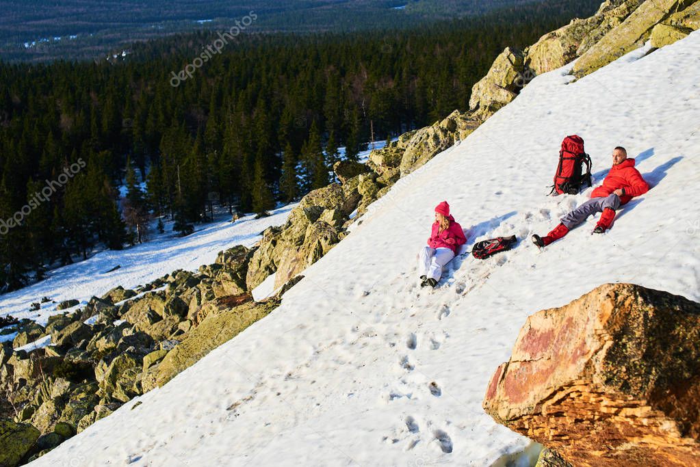 tourist couple in love relaxing while lying on snowy slope in mountains at sunny day 