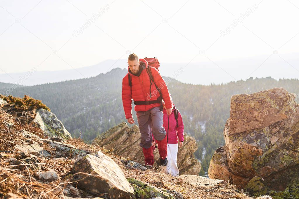 man with woman climbing on slope with mountains on background 