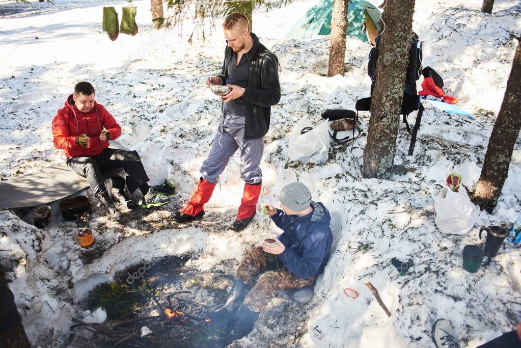 backpackers eating near bonfire in spring forest, hike concept  