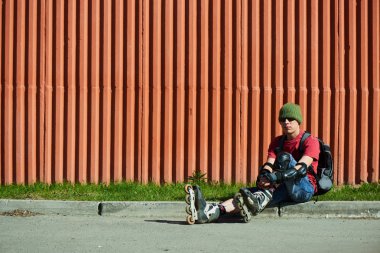 Tekerlekli paten kırmızı duvar karşı kaldırıma oturan adam