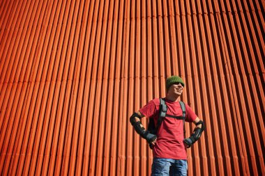 ekipman ile kırmızı duvar arka bina üzerinde sırt çantası duran adam 