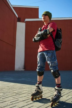 Tekerlekli paten ayakta kırmızı binalar yakın çapraz kolları olan kendine güvenen adam 