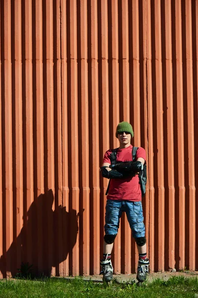 confident man with crossed arms in roller skates standing near red wall