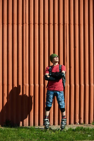 confident man with crossed arms in roller skates standing near red wall