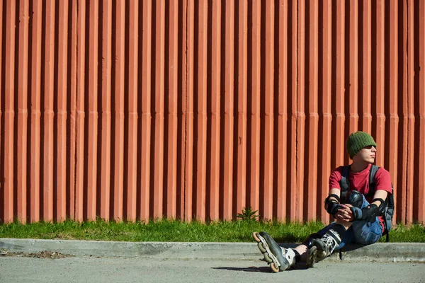 man in roller skates sitting on curb against red wall