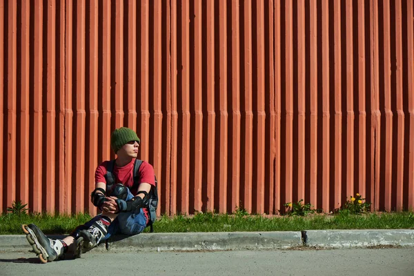 man in roller skates sitting on curb against red wall