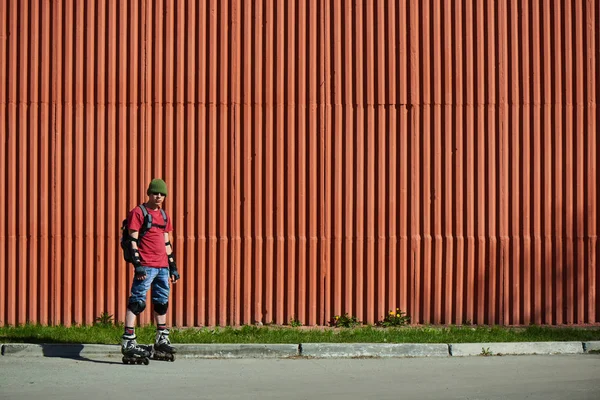 confident man in roller skates standing near red building