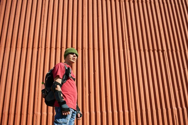 ekipman ile kırmızı duvar arka bina üzerinde sırt çantası duran adam 