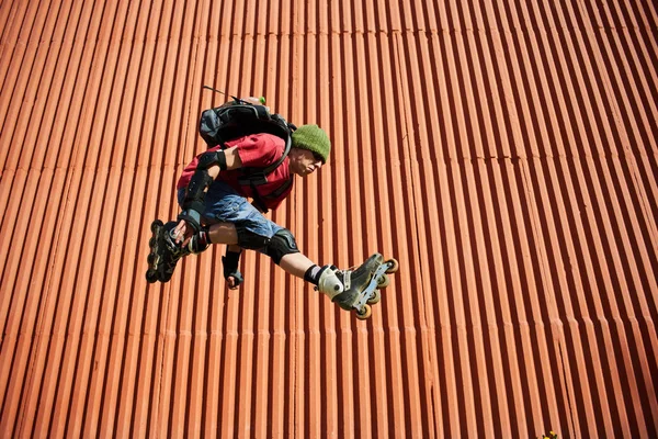 man in roller skates jumping against red wall outdoor