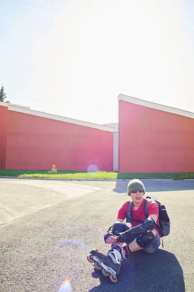 güneşli bir gün binaya yakın asfalt üzerinde oturan paten şık patenci 