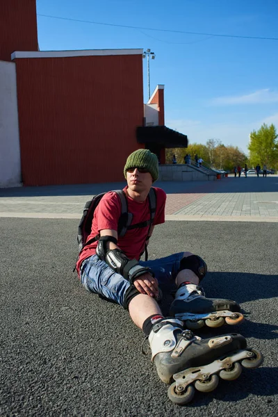 portrait of man in roller skaters sitting on pavement