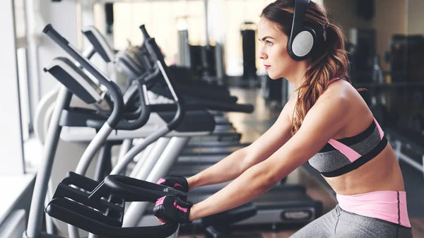 Atletisk Ung Kvinna Hörlurar Träna Motionscykel Gymmet — Stockfoto