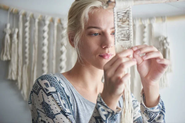 blonde woman weaving element of macrame decoration, female hobby concept