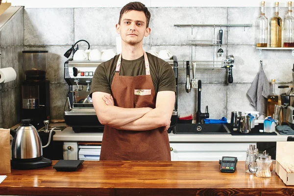 male waiter with crossed arms standing at workplace in coffee shop