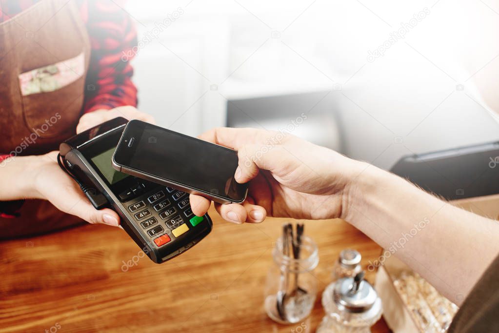 cashier holding terminal and customer contactless paying by phone at coffee shop