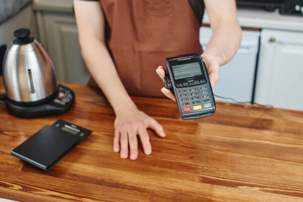 cashier holding card payment terminal over wooden surface of bar 