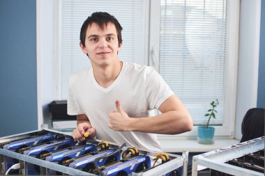 kameraya bakarak ve başparmak cryptocurrency ofiste çıkarım için farm yakınındaki dururken gösterilen genç adam 