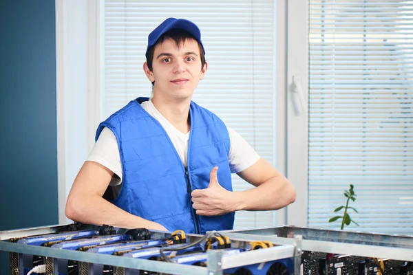 kameraya bakarak ve başparmak cryptocurrency ofiste çıkarım için farm yakınındaki dururken gösterilen genç adam 