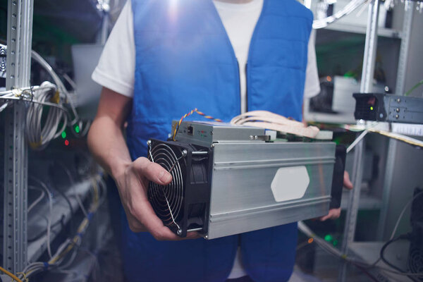 male worker holding bitcoin mining equipment in hands on cryptocurrency farm
