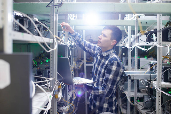 концентрированный работник держит ноутбук при установке фермы по добыче криптовалют
 