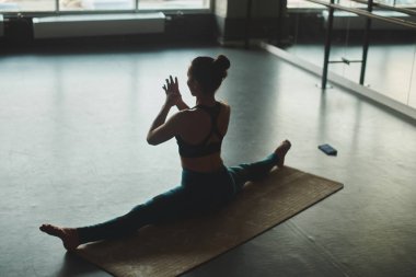 kadın ise dize üzerinde oturan ve pratik yoga mat spor salonunda esnekliğini göstererek