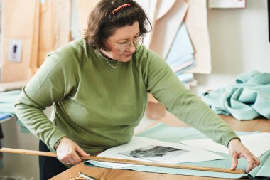 atelier giysilerle oluşturulması üzerinde çalışırken dikiş kalıpları kullanarak terzi konsantre