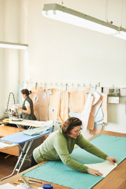 atelier giysilerle oluşturulması üzerinde çalışırken dikiş kalıpları kullanarak terzi konsantre