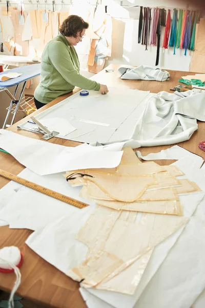 young woman tailor and drawing model of clothes in atelier