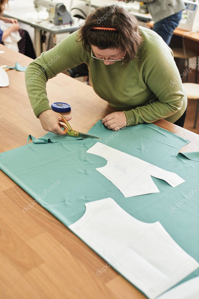 dressmaker with scissors cutting cloth on table 