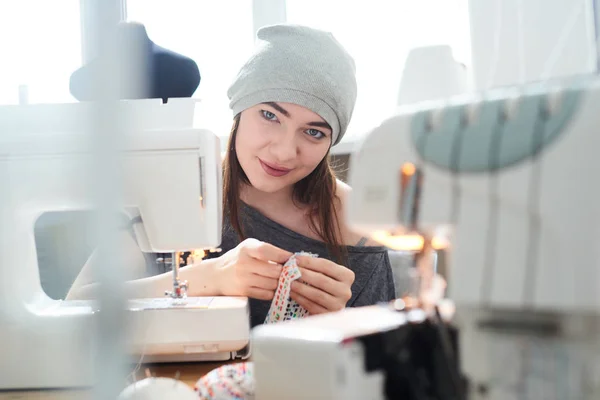 seamstress looking at camera while tailoring cloth in atelier